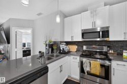 Modern kitchen featuring white shaker cabinetry, stainless steel appliances, a dark tile backsplash, and light gray countertops - 