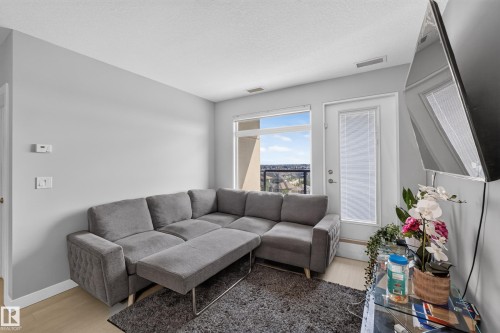 Living area featuring light wood-finish flooring, light grey walls, and a large window with an outdoor landscape - 706 5151 Windermere Boulevard, Edmonton, AB 