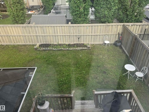 Fenced backyard featuring a raised garden bed, green lawn, and a multi-level wooden deck - 1019 175 Street, Edmonton, AB 