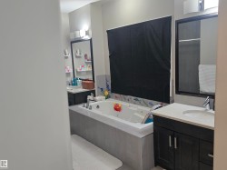 Bathroom featuring a built-in jetted tub with tile surround, dual vanity areas with dark wood cabinetry and light countertops, and individual framed mirrors with integrated lighting - 