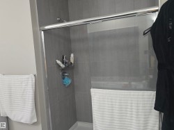 Walk-in shower featuring gray subway tile walls, a chrome showerhead, and a clear glass sliding door - 