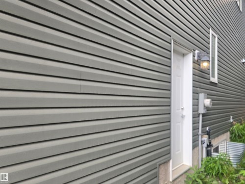 Gray horizontal siding exterior with a white entry door, an exterior wall sconce, and a rectangular window - 1019 175 Street, Edmonton, AB 