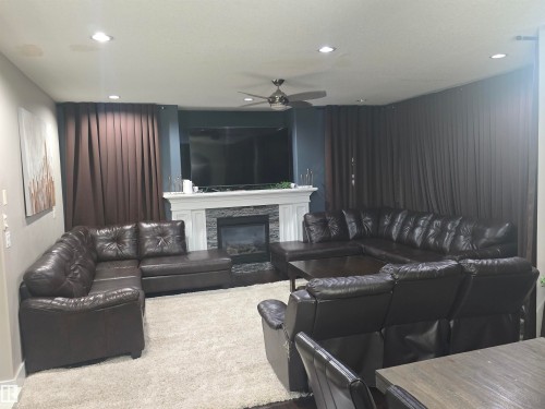 Living area featuring a fireplace with a white mantel and stone surround, recessed lighting, and a ceiling fan - 1019 175 Street, Edmonton, AB 