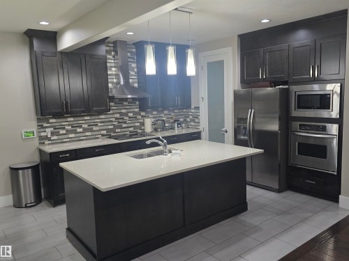 Kitchen featuring dark wood cabinetry, a central island with a light-toned countertop, a tile backsplash, stainless steel appliances, and recessed lighting - 1019 175 Street, Edmonton, AB 