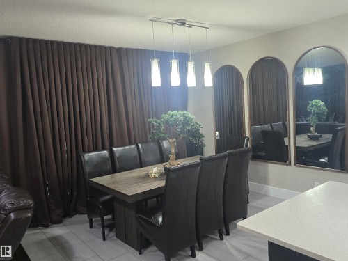 Dining area featuring a linear pendant light fixture with four glass shades, an expansive brown curtain wall, and three arched wall mirrors - 1019 175 Street, Edmonton, AB 