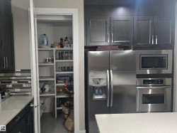Kitchen featuring stainless steel refrigerator, built-in microwave, wall oven, dark wood cabinetry, and a walk-in pantry with extensive shelving - 
