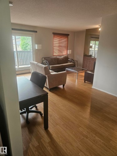 Open-concept living space featuring wood-finish flooring, light-toned walls, a sliding glass door providing natural light, and a private balcony - 10838 108 Street Nw, Edmonton, AB 
