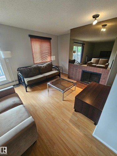 Living area featuring wood-finish flooring, a brick-front fireplace, and a mirrored accent wall - 10838 108 Street Nw, Edmonton, AB 