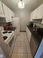 Galley kitchen featuring white cabinetry, dark countertops, white appliance package, stainless steel dishwasher, and a tiled floor - 