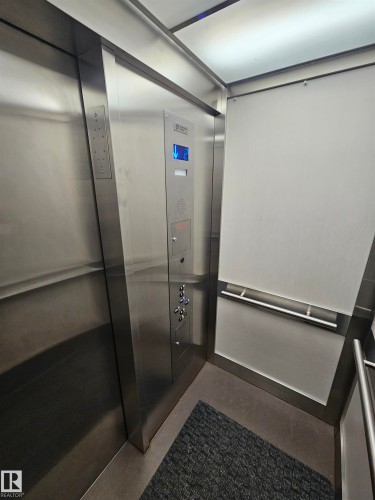 Elevator interior featuring brushed stainless steel walls, integrated control panel with digital floor indicator, corner handrail, and overhead panel lighting - 10838 108 Street Nw, Edmonton, AB 