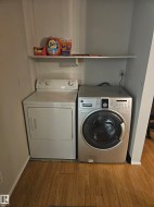 Dedicated laundry area featuring wood-finish flooring, a white wall-mounted shelf, and light gray walls - 