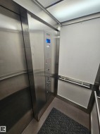 Elevator interior featuring brushed stainless steel walls, integrated control panel with digital floor indicator, corner handrail, and overhead panel lighting - 