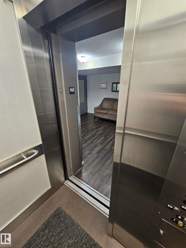 Stainless steel elevator interior opening to a hallway featuring wood-finish flooring and a ceiling-mounted light fixture - #206 10838 108 Street Nw, Edmonton, AB - Indoor Photo Showing Other Room