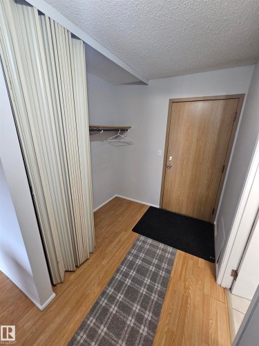 Entryway featuring wood-finish flooring, light grey wall paint, and a built-in closet with accordion doors - 10838 108 Street Nw, Edmonton, AB 