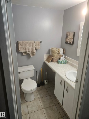 Compact bathroom featuring a white toilet, tile flooring, a single vanity with storage cabinetry, an integrated sink, and a wall-mounted mirror - 10838 108 Street Nw, Edmonton, AB 