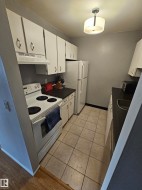 Compact kitchen featuring extensive upper and lower cabinetry, white appliances including a range and refrigerator, dark countertops, and tile flooring - 