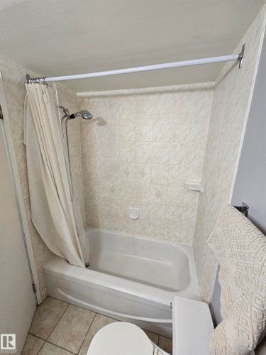 Bathroom featuring a white bathtub, ceramic tile surround, and an integrated shower head - 10838 108 Street Nw, Edmonton, AB 