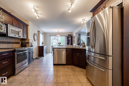 Kitchen featuring stainless steel appliances, dark wood-finish cabinetry, tile flooring, and track lighting - 5820 7 Avenue Sw, Edmonton, AB - Indoor Photo Showing Kitchen