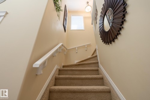 Carpeted stairway featuring a white handrail, light beige wall paint, and natural light from an upper-level window - 5820 7 Avenue Sw, Edmonton, AB - Indoor Photo Showing Other Room
