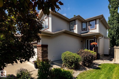 Two-story residence featuring light-toned siding, dark window trim, a stone-clad pillar, an integrated garage, and landscaped front yard with grass and shrubbery - 5820 7 Avenue Sw, Edmonton, AB - Outdoor