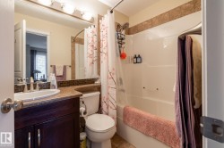 Bathroom featuring a dark wood-finish vanity with a single basin sink, a large mirror, a tiled backsplash, and a combination tub/shower with a tiled surround - 