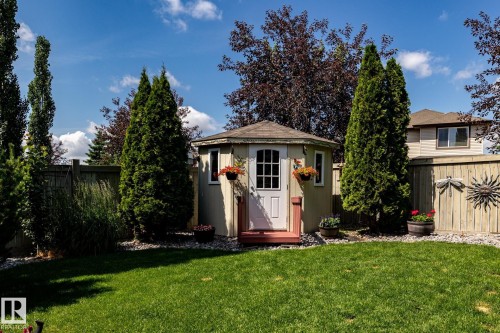 Expansive backyard featuring a manicured lawn and a hexagonal storage shed with a shingled roof, white door, and red-painted steps - 5820 7 Avenue Sw, Edmonton, AB - Outdoor