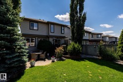 Manicured backyard featuring a paver patio, a lush lawn, mature trees, and privacy fencing - 