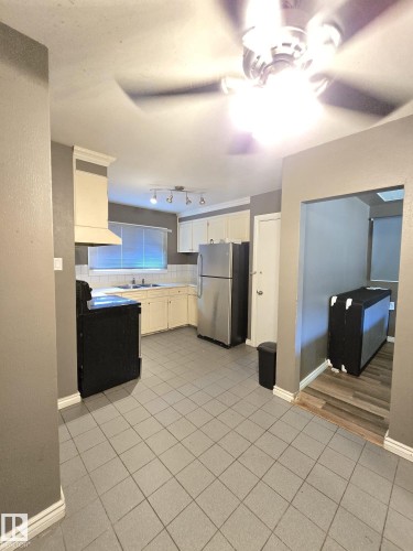Functional kitchen featuring white cabinetry, a stainless steel refrigerator, and an integrated range hood - 9616 63 Avenue, Edmonton, AB 