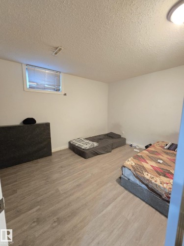 Spacious room featuring light wood-finish flooring, white walls, and a window with blinds - 9616 63 Avenue, Edmonton, AB 