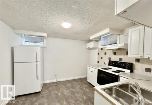 Functional kitchen space featuring white cabinetry, a dual basin stainless steel sink, tile backsplash, and an electric stove with range hood - 9616 63 Avenue, Edmonton, AB 