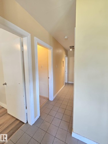 Hallway featuring light-toned tile flooring, light-colored walls, white trim, and a ceiling-mounted light fixture - 9616 63 Avenue, Edmonton, AB 