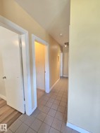 Hallway featuring light-toned tile flooring, light-colored walls, white trim, and a ceiling-mounted light fixture - 