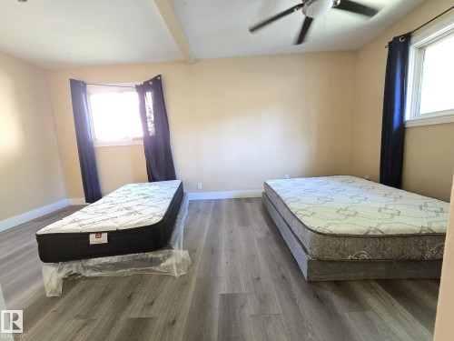 Spacious room featuring wood-finish flooring, two windows, and a ceiling fan - 9616 63 Avenue, Edmonton, AB 