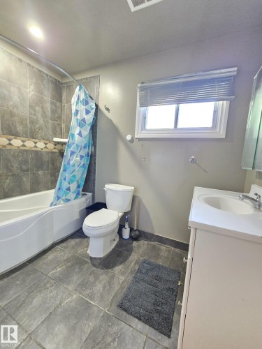 Bathroom featuring a white bathtub with a tiled shower surround, a white toilet, and a vanity with an integrated sink - 9616 63 Avenue, Edmonton, AB 
