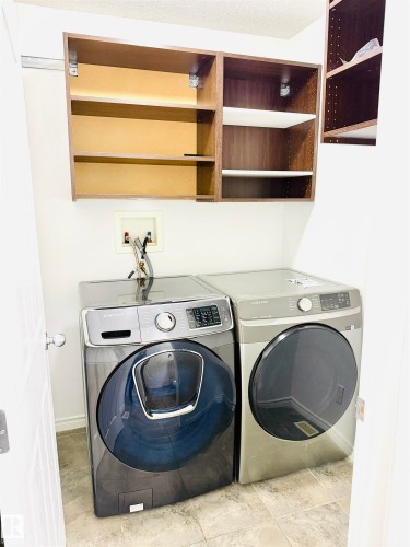 Laundry area featuring wood-finish wall cabinetry with adjustable shelving, a neutral tile floor, and white walls - 3120 25 Avenue, Edmonton, AB 
