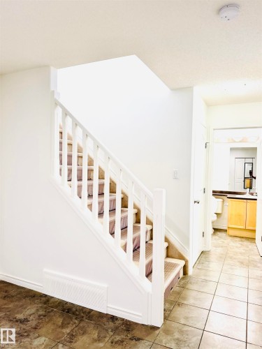 Staircase with carpeted treads and white wood balusters, complemented by a stone-look tiled floor and a built-in baseboard return air vent - 3120 25 Avenue, Edmonton, AB 