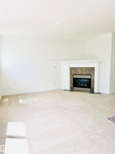 Living area featuring a gas fireplace with a stone surround and white mantel, recessed ceiling lighting, and light-colored carpeting - 3120 25 Avenue, Edmonton, AB 