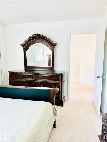 Carpeted interior space with white walls and trim, featuring a partial view of an open doorway and a portion of a bed frame - 3120 25 Avenue, Edmonton, AB 