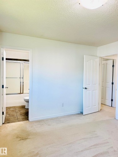 Carpeted room with a full bathroom featuring a white tub, sliding glass shower doors, and tiled flooring - 3120 25 Avenue, Edmonton, AB 