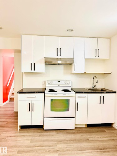 Kitchenette featuring white cabinetry, dark countertops, a stainless steel sink, a white electric range, and wood-finish flooring - 3120 25 Avenue, Edmonton, AB 