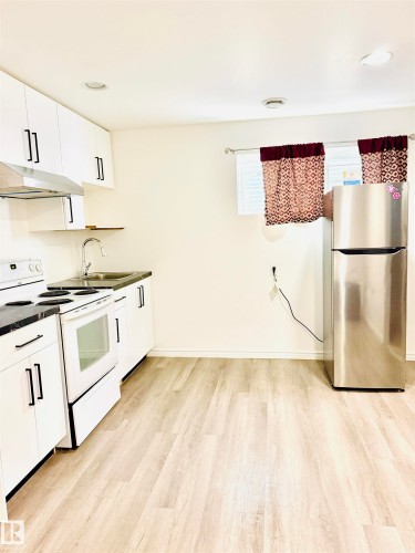 Compact kitchen featuring white cabinetry with black hardware, dark countertops, and stainless steel appliances - 3120 25 Avenue, Edmonton, AB 