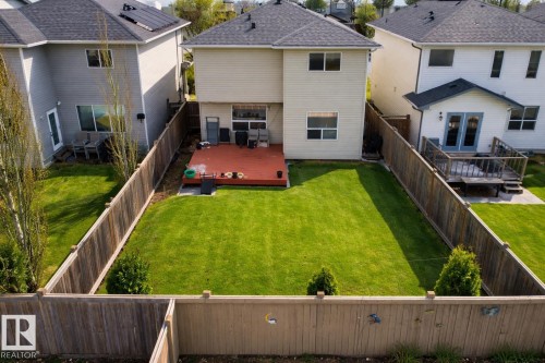 Expansive fenced backyard featuring a manicured lawn, red-toned wood deck, and established perimeter trees - 3120 25 Avenue, Edmonton, AB 