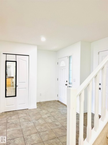 Entryway featuring tile flooring, a white front door with decorative glass, and a white baluster staircase - 3120 25 Avenue, Edmonton, AB 