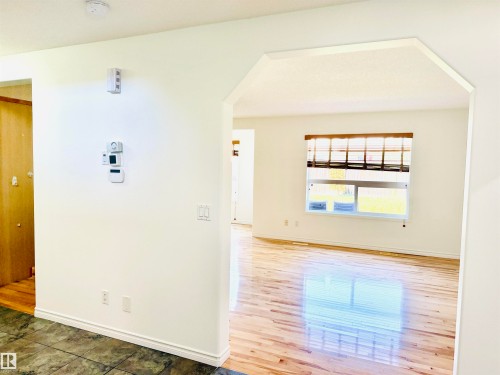 Archway entrance opening into a room featuring wood-finish flooring, a window with horizontal blinds, and neutral wall tones - 3120 25 Avenue, Edmonton, AB 
