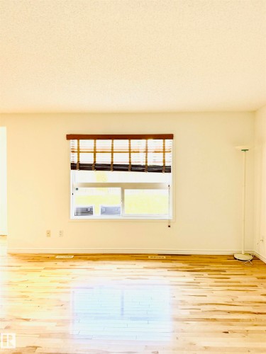 Open interior space with light-tone wood flooring, white baseboards, and a window featuring a wood-slat blind - 3120 25 Avenue, Edmonton, AB 
