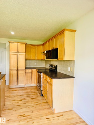Kitchen featuring light wood cabinetry, dark countertops, a tiled backsplash, stainless steel range, and wood-finish flooring - 3120 25 Avenue, Edmonton, AB 