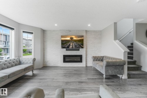 Spacious living area featuring grey wood-finish flooring and a contemporary electric fireplace with a stacked stone-look surround - 17724 58 Street Nw, Edmonton, AB 