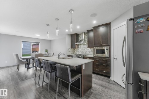 Open-concept kitchen featuring an island with a light-toned countertop, wood-finish flooring, dark wood cabinetry, a tiled backsplash, and recessed lighting - 17724 58 Street Nw, Edmonton, AB 