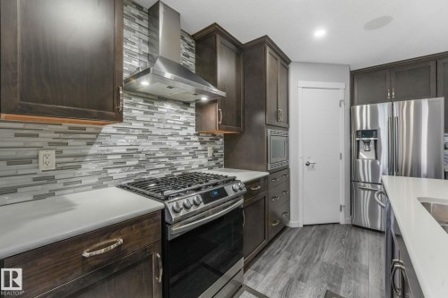 Contemporary kitchen featuring stainless steel appliances, dark wood-finish cabinetry, a subway tile backsplash, light-toned countertops, and wood-finish flooring - 17724 58 Street Nw, Edmonton, AB 