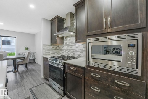 Kitchen featuring dark wood cabinetry, stainless steel appliances, light countertops, and a tiled backsplash - 17724 58 Street Nw, Edmonton, AB 